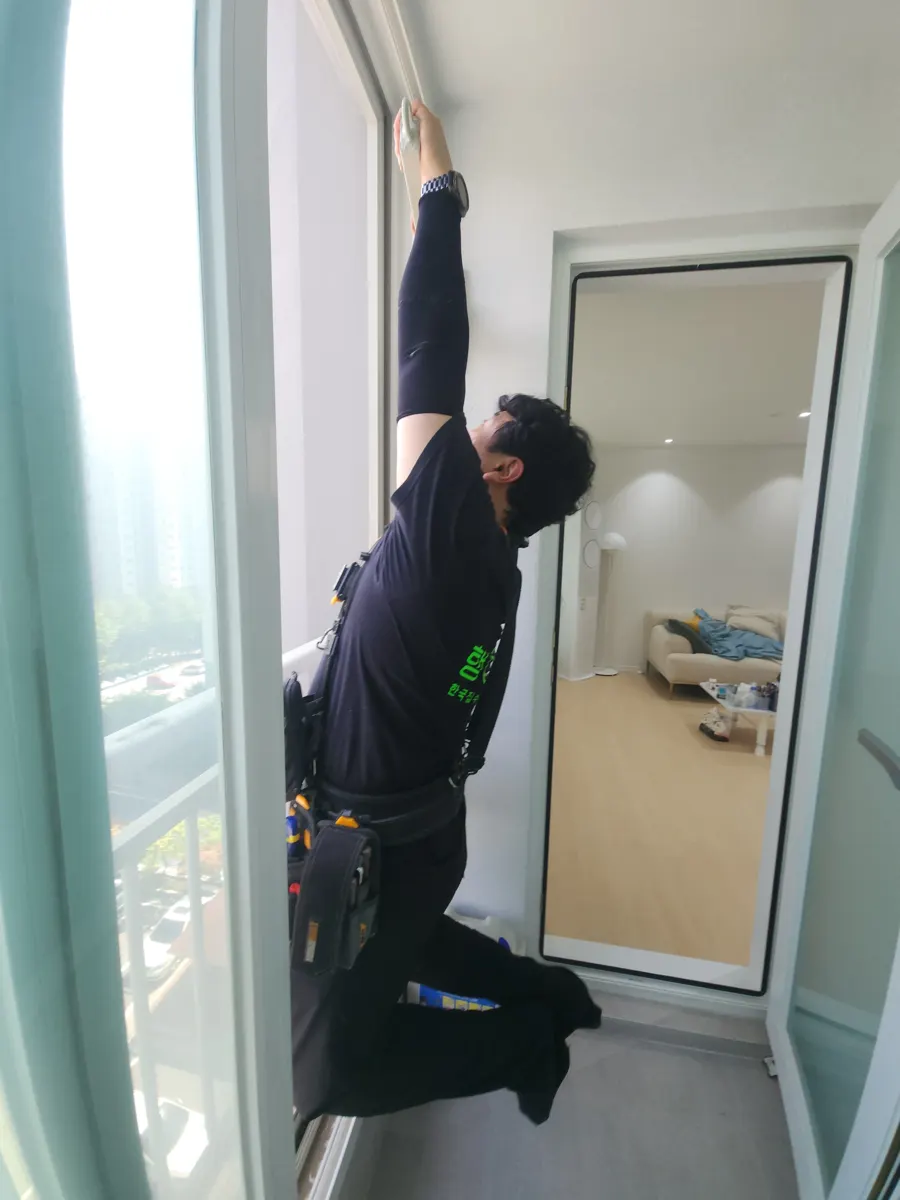 광명 완강기 설치 시공 기사가 창가 벽면 상부에서 작업하는 모습